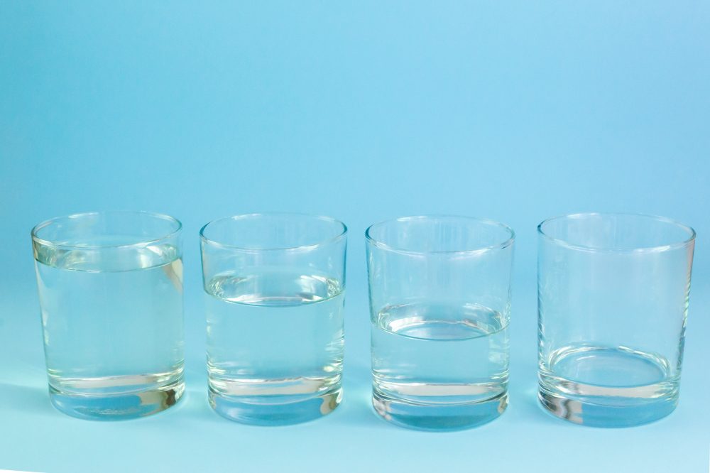 Four glass glasses with water stand on a blue background. Waste water concept. Horizontal orientation.